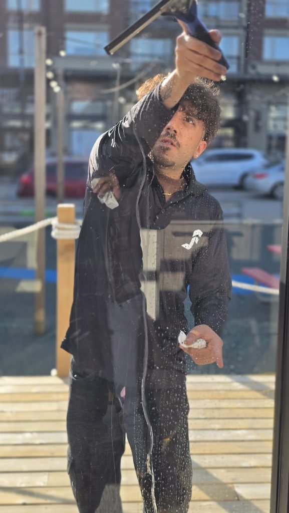 A man wearing a black dress having JF logo on the right cleaning a window. 